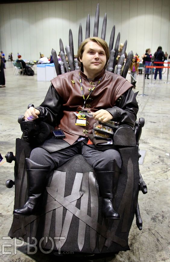 Young man in a powerchair wearing clothing from the series "Game of Thrones". His wheelchair is fashioned to look like the Iron Throne