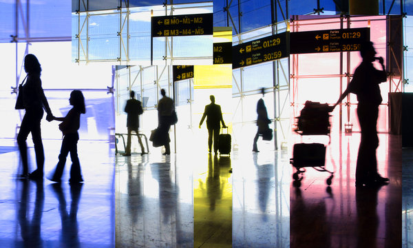 shadows of people inside an airline terminal with suitcases and departure signs